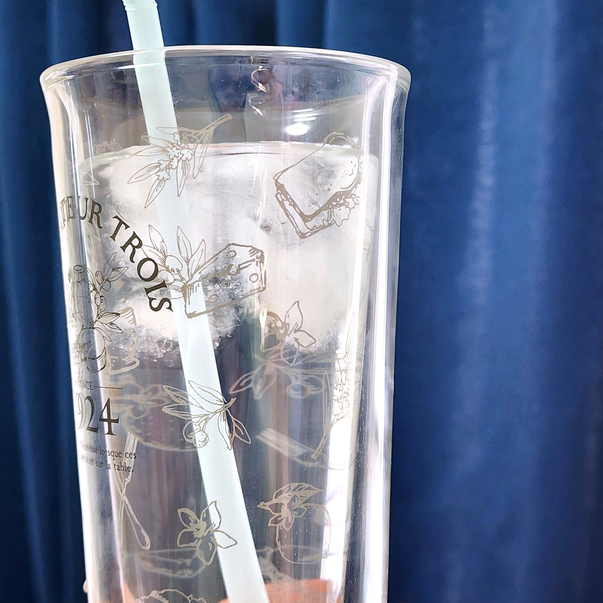透明なカップに刻まれた花の模様と、ストローが差し込まれた飲み物が写っている。
