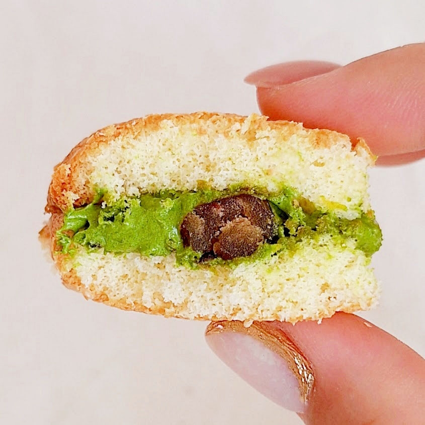 手に持たれたピスタチオとチョコチップが挟まれたマカロンのクローズアップ写真。