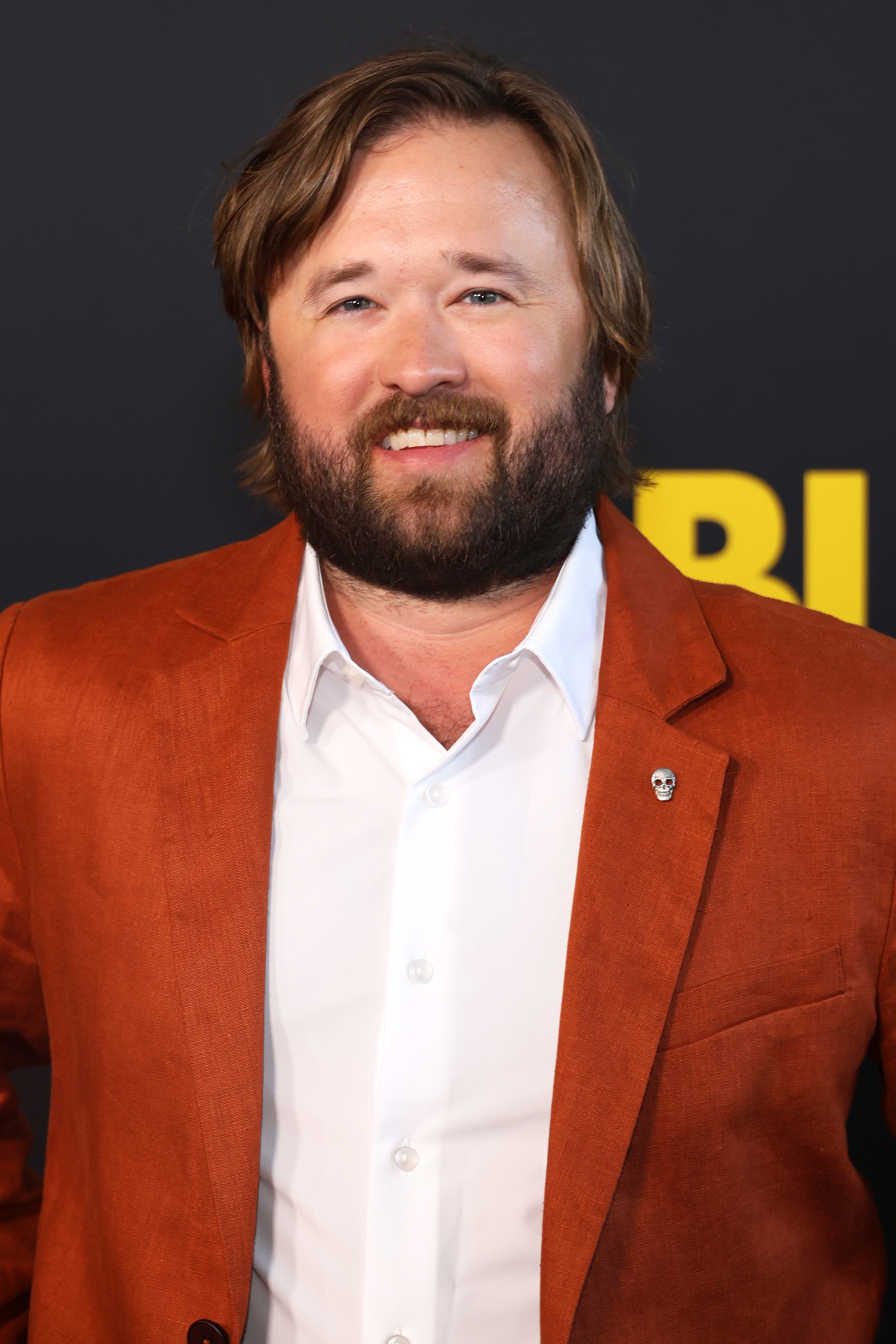 Haley Joel Osment with a beard and medium-length hair in a stylish rust-colored blazer and white shirt at a formal event