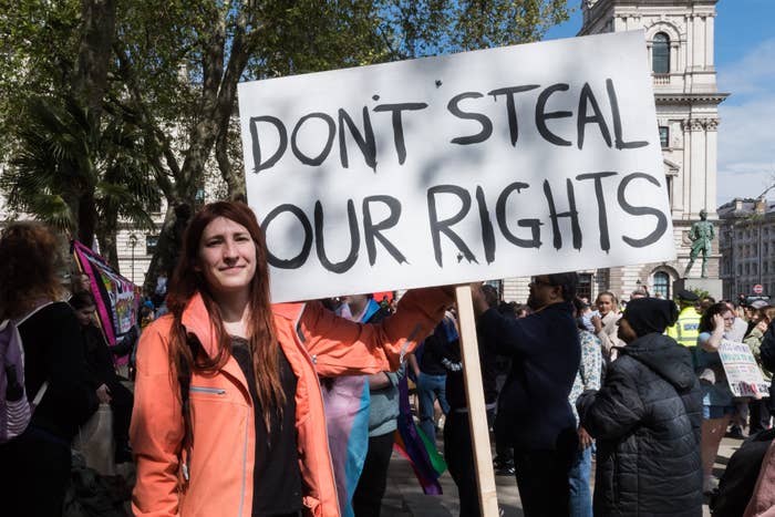 Person holding a "Don't Steal Our Rights" sign at a protest, surrounded by a crowd and trees in the background