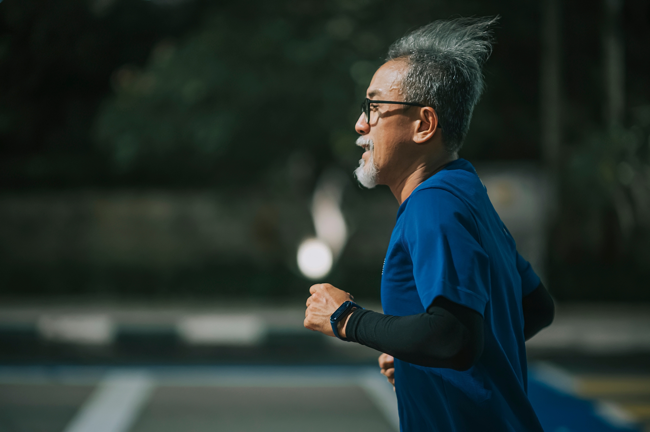 En eldre voksen jogger utendørs, iført en kortermet atletisk skjorte og smartwatch, og understreker en aktiv livsstil