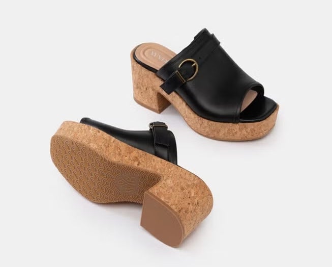 Two black open-toe platform sandals with cork soles and buckle details, positioned on a neutral background