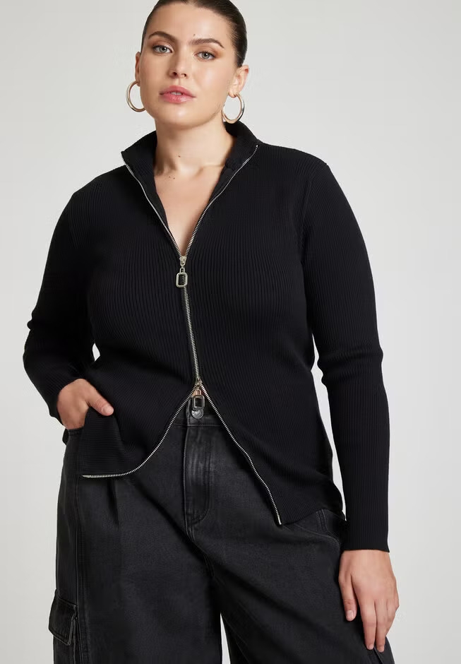 Person wearing a zip-up black sweater with a ribbed texture and hoop earrings, modeling for a shopping feature