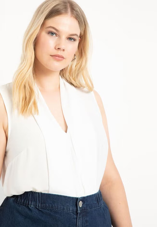 Person in a sleeveless, v-neckline top and high-waisted jeans, posing confidently