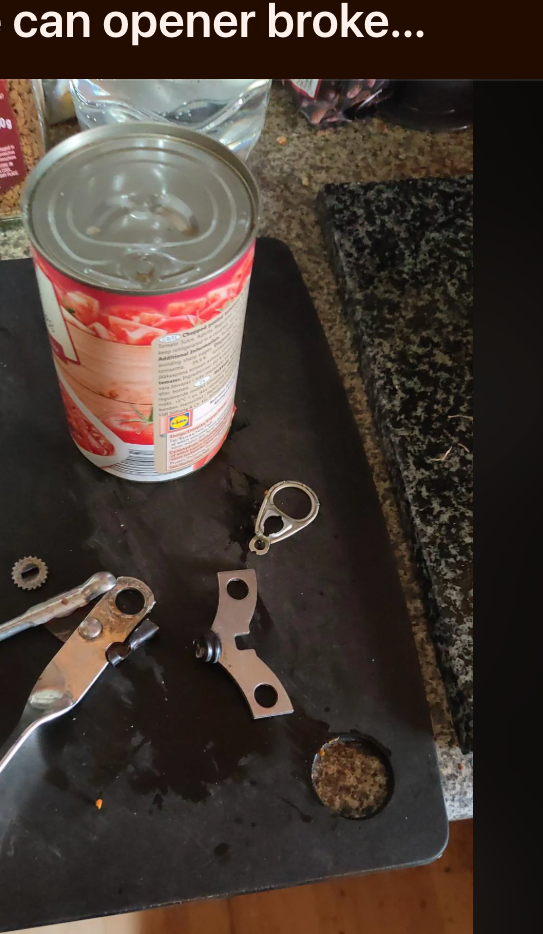 A can with a broken ring pull and an unusable can opener on a countertop, highlighting a frustrating kitchen experience. Reddit post is visible in the background