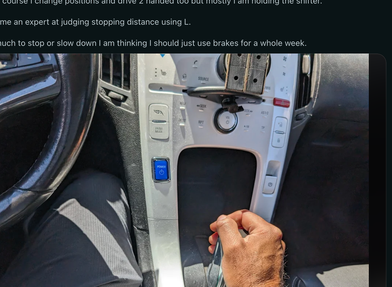 A person's hand is on a car's gear shift in a vehicle interior. Reddit page visible in the background shows a discussion about driving experiences