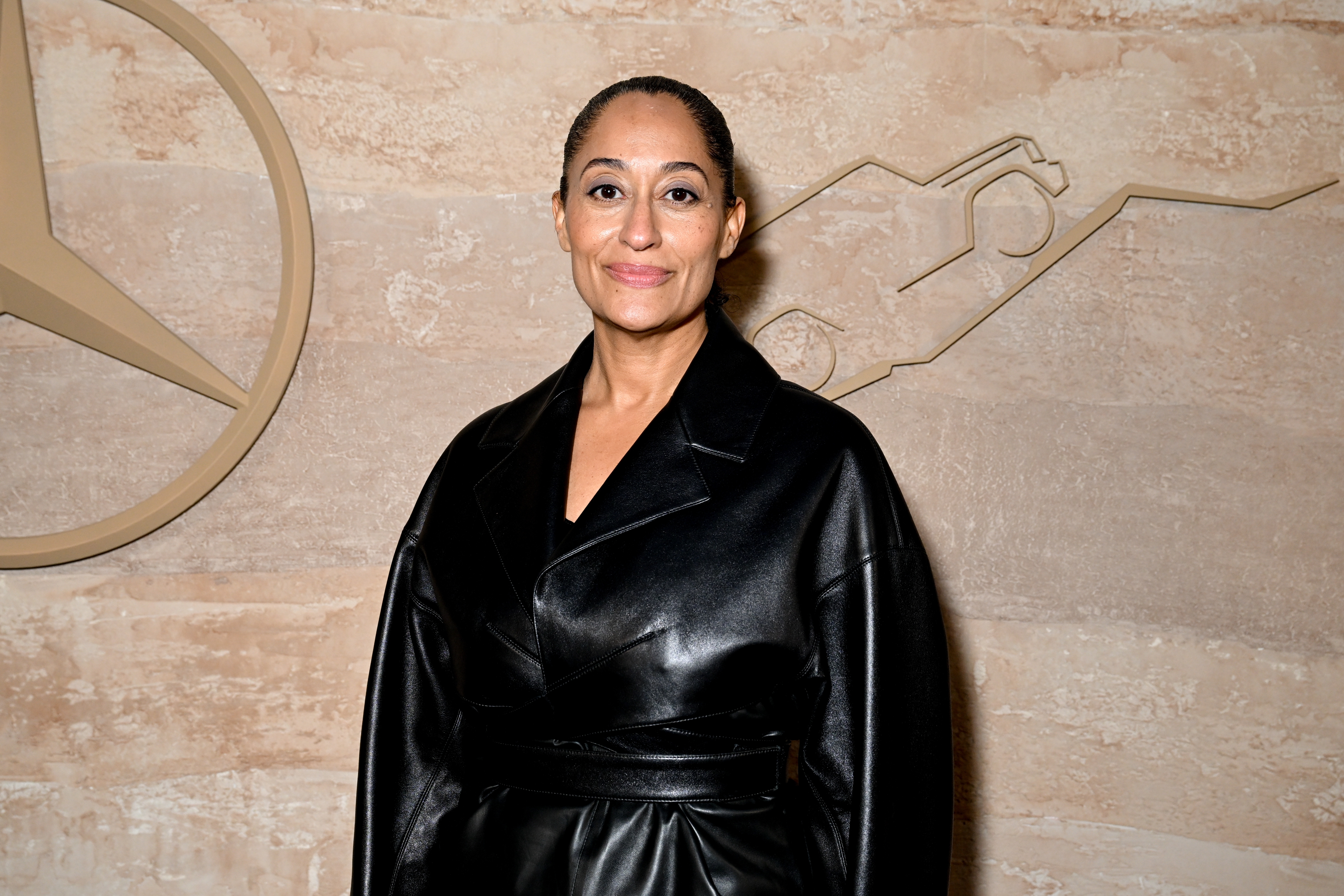Tracee Ellis Ross wearing a sleek leather coat, standing in front of an abstract wall design