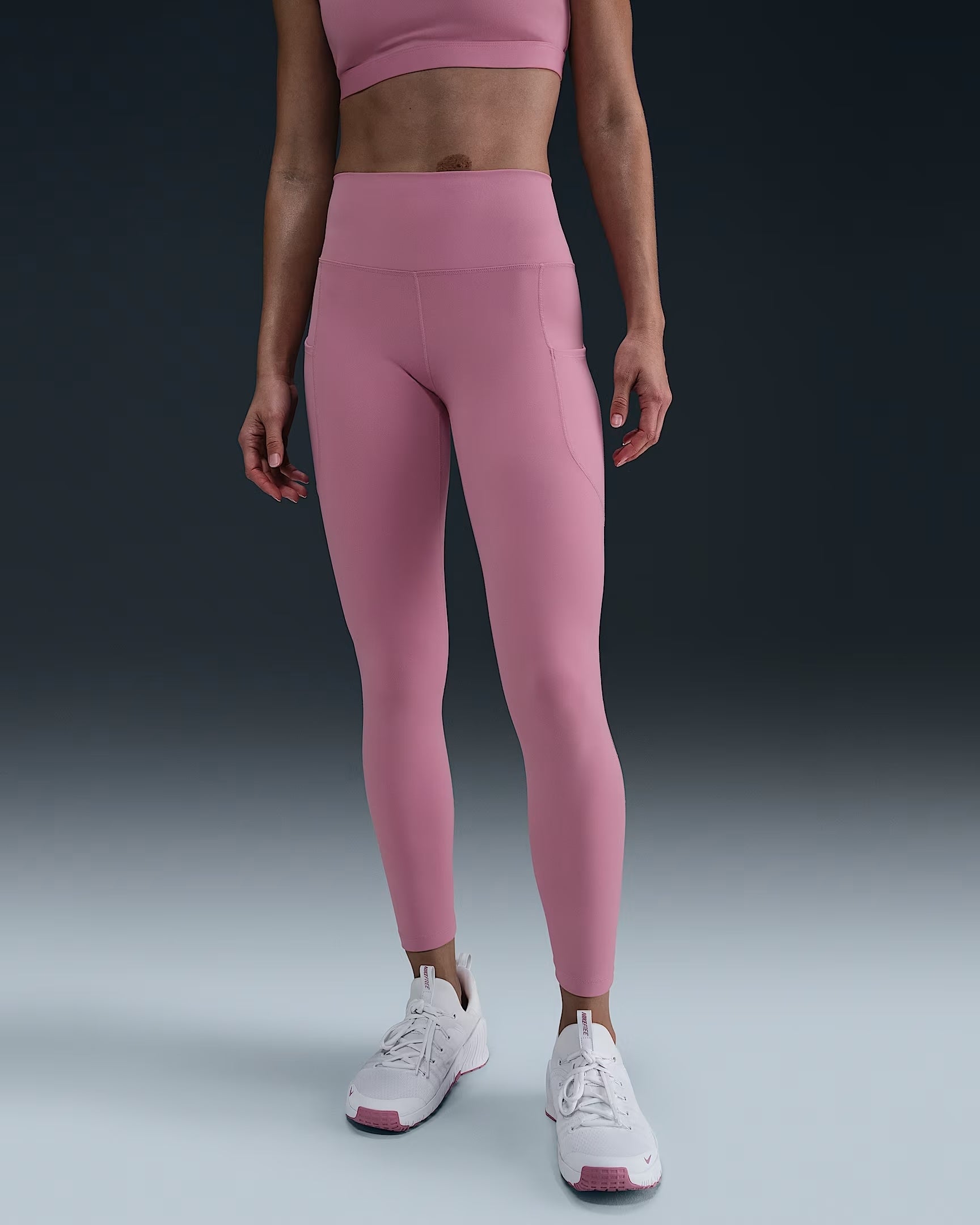 Orang pemodelan pakaian pink diatur dengan latar belakang polos, menampilkan legging dan crop top dengan sepatu putih
