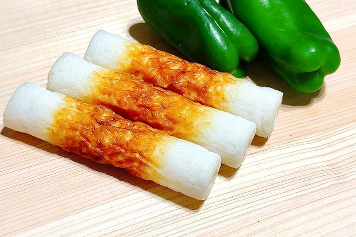 まな板の上に、白と茶色の焼き目があるちくわ3本と、緑色のピーマン2個が置かれています。