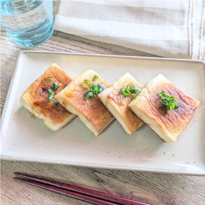 豆腐のステーキが4切れ、青ネギがトッピングされ、白い皿に盛られている。横にはガラスの水と赤い箸。