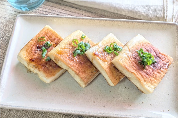 皿に盛られた焼き豆腐、ネギがトッピングされたオシャレなプレゼンテーション。隣にガラスの水。