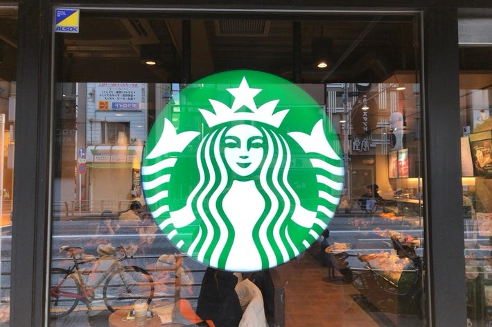 スターバックスのロゴがガラス窓に設置されている店舗の外観。背景に道と自転車が見える。