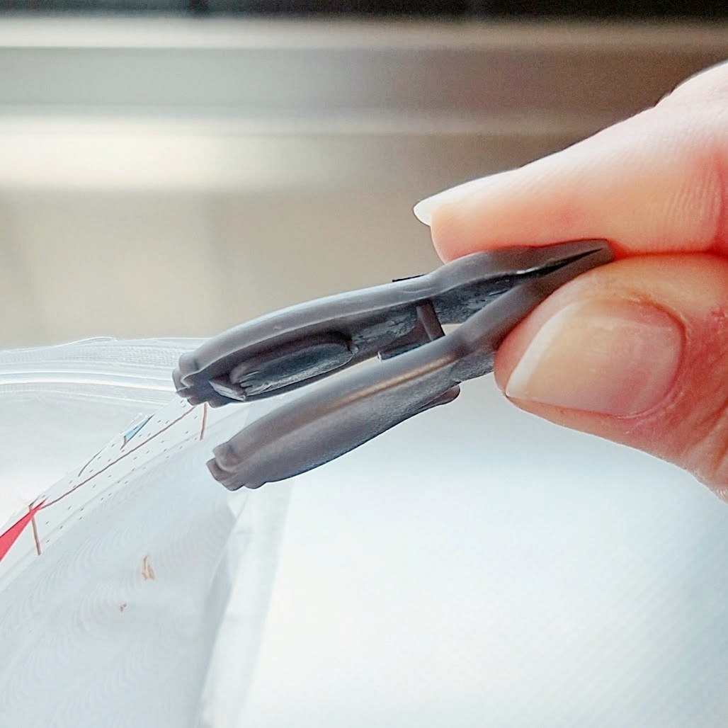 手に持たれた小さなグレーのクリップ、透明な袋を閉じる場面。