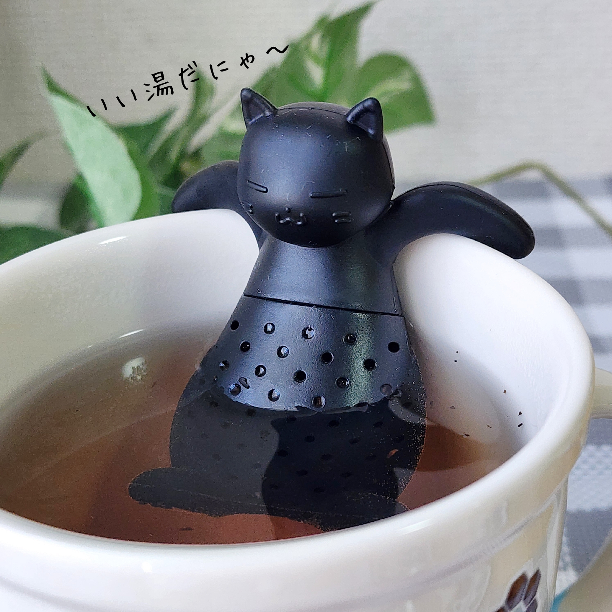 猫型のティーバッグホルダーがカップに浸かっている。リラックスした表情をしていて、楽しそうに見えるイラスト付き。