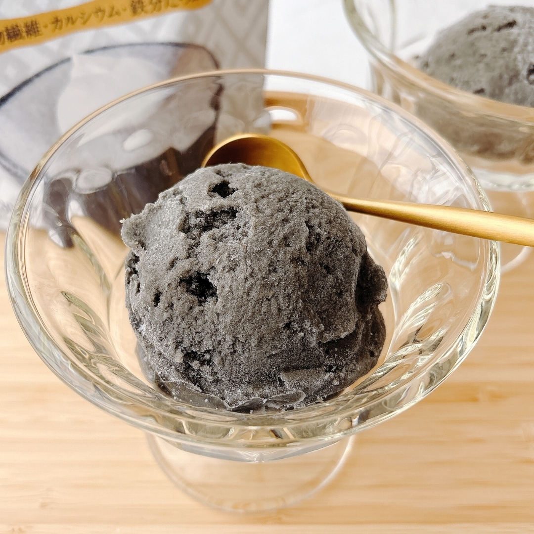 ガラスの器に盛られた黒ごまアイスクリームとゴールドのスプーン。背景にアイスのパッケージが見える。