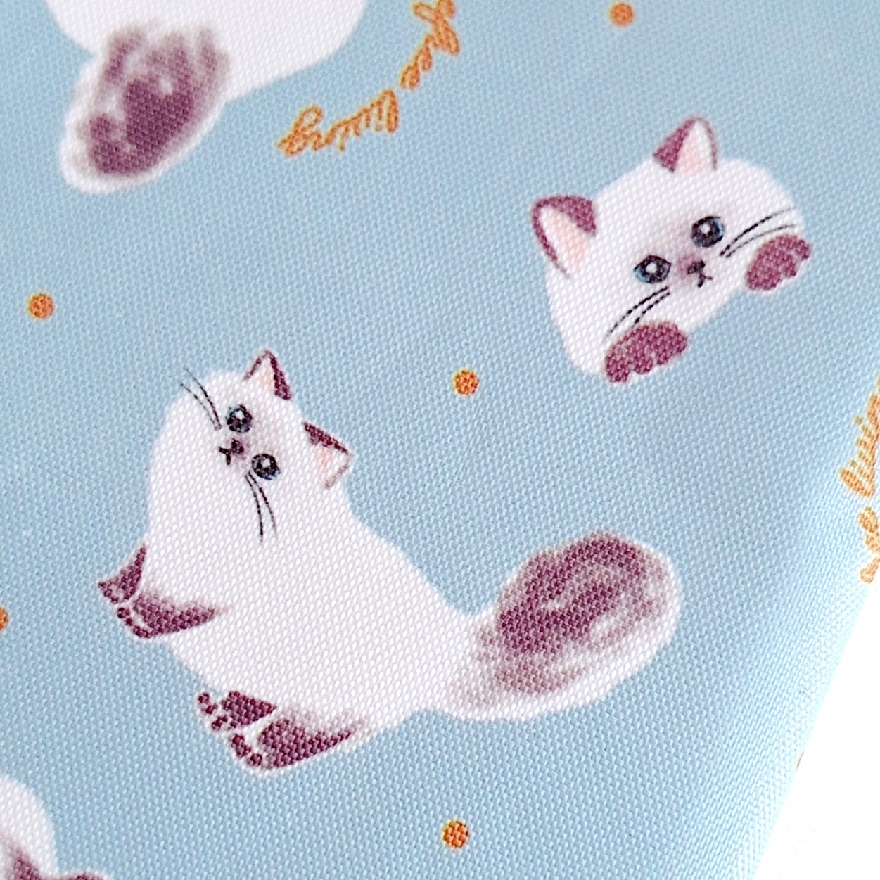 白い猫のイラストが散りばめられているデザインの布地。猫はふんわりした毛並みで可愛らしい表情をしている。