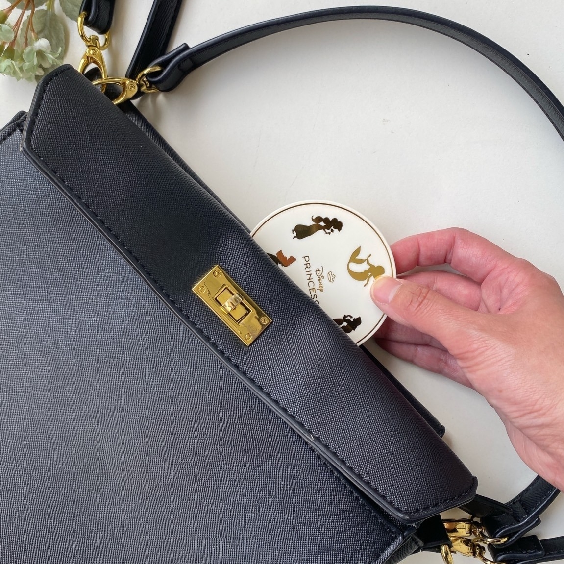 黒のハンドバッグにディズニープリンセスのイラストが描かれたコンパクトを入れる様子。