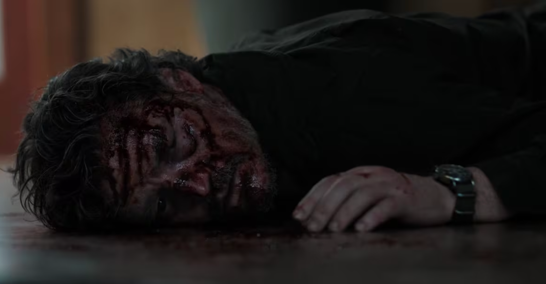 Hombre herido yace en el suelo con el rostro cubierto de sangre y tierra. Lleva una camisa oscura y un reloj. Escena dramática de una serie o película