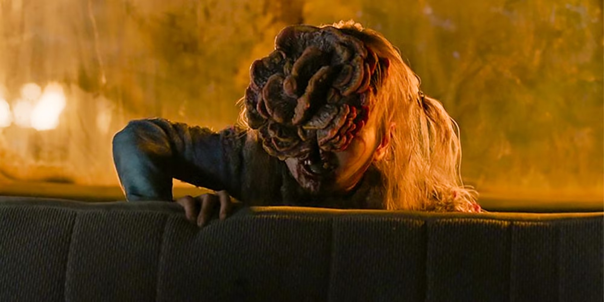 Una criatura con un rostro lleno de deformidades se asoma sobre el respaldo de un asiento en una escena de terror