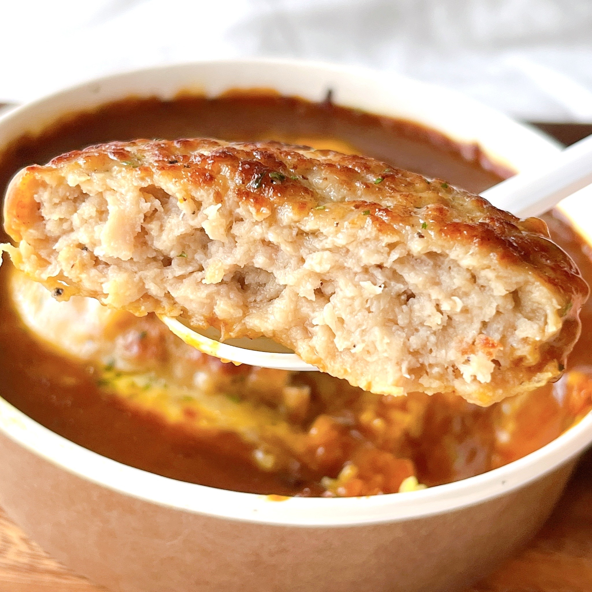 ハンバーグカレーのスプーンすくい上げショット。カレーソースの中にジューシーなハンバーグ。