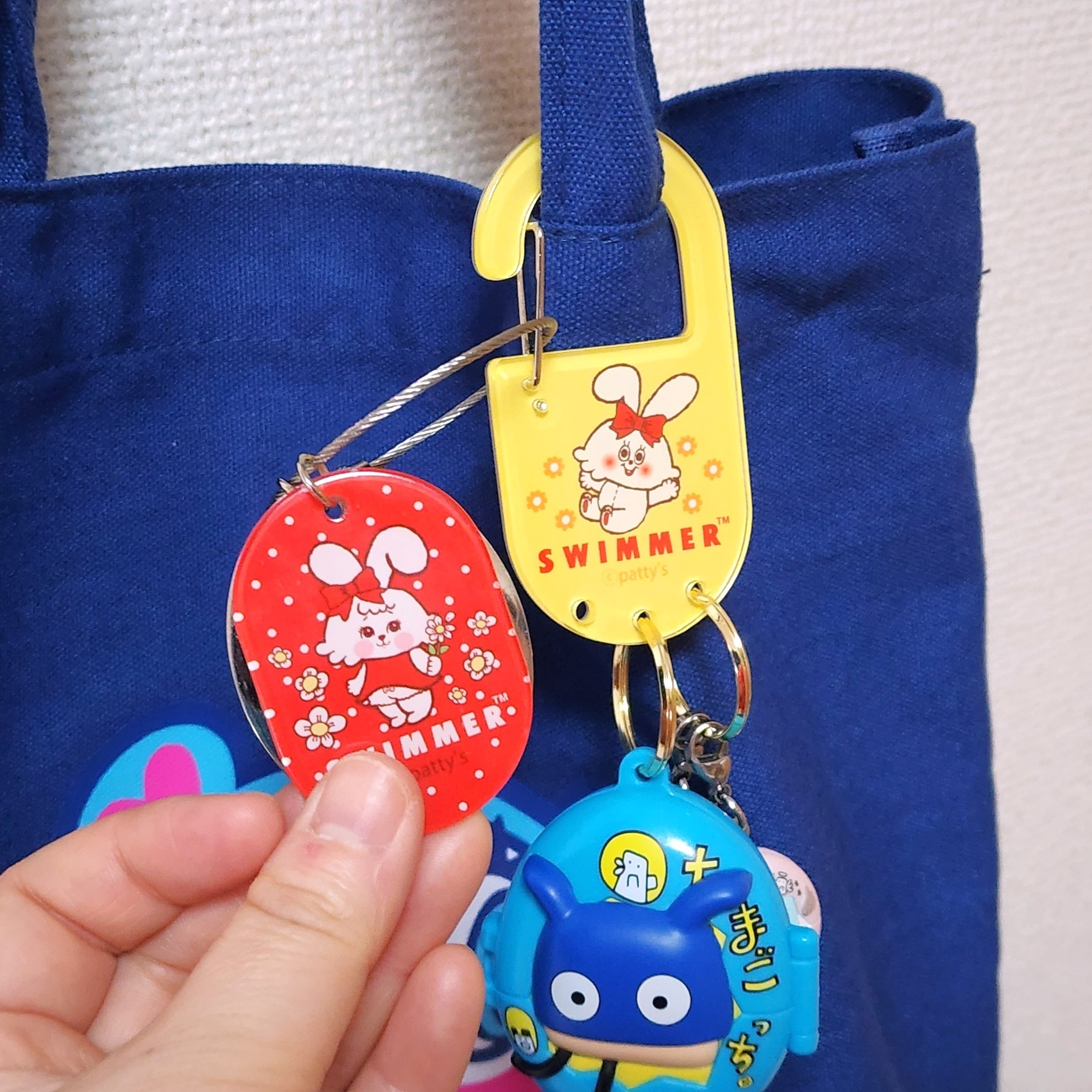 青いバッグに吊るされた動物キャラクターのキーホルダー。手で一つ持ち上げている。
