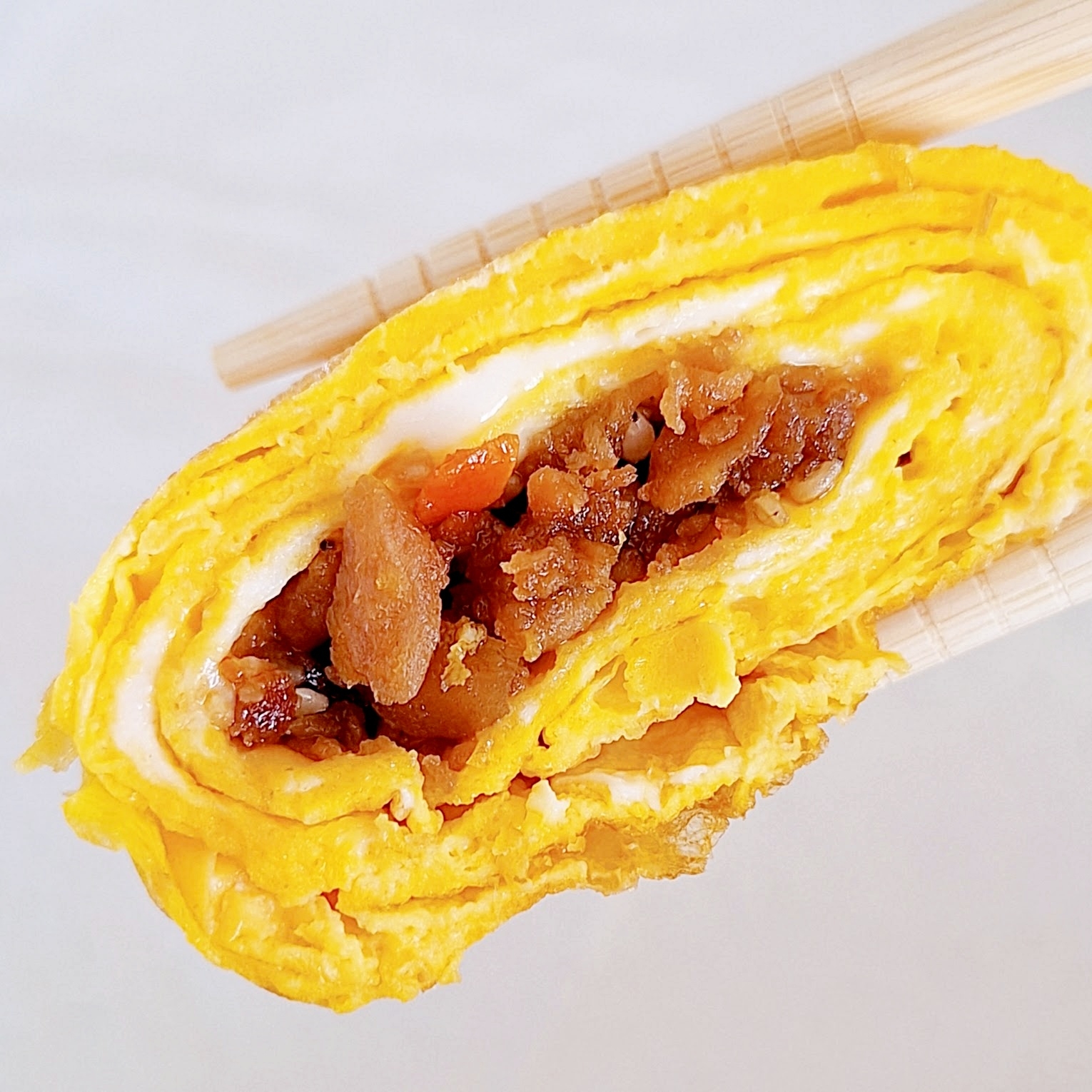 卵焼きで巻かれた具材入り寿司が箸で持ち上げられている。