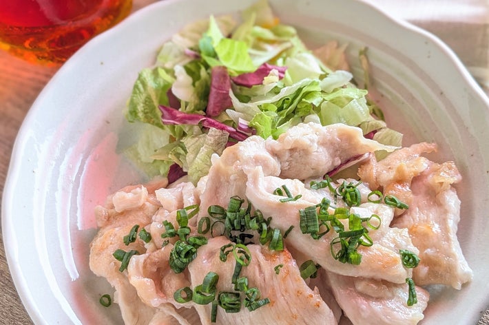 サラダとネギを載せた肉料理の皿。横に飲み物と小さなソースの入った器がある。