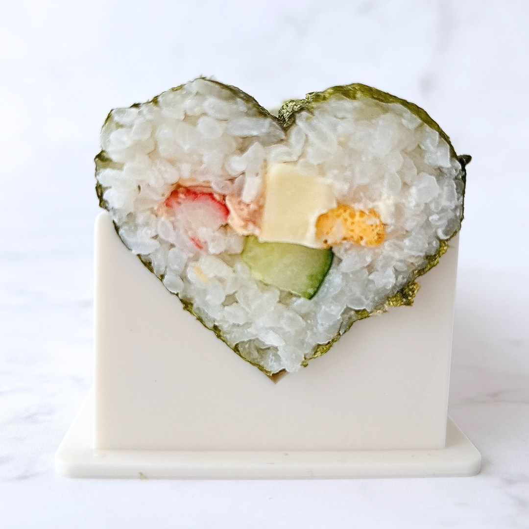ハート型の寿司ロール。具材にはカニ風味かまぼこ、チーズ、きゅうりなどが入っている。白い台に立てられている。