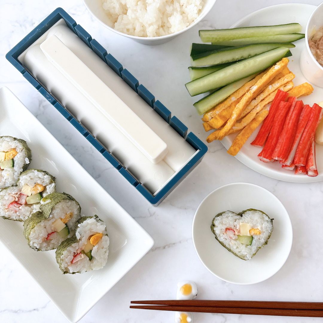 寿司キットと具材(カニカマ、キュウリなど)、巻いた寿司、心形の寿司がテーブルに置かれている。