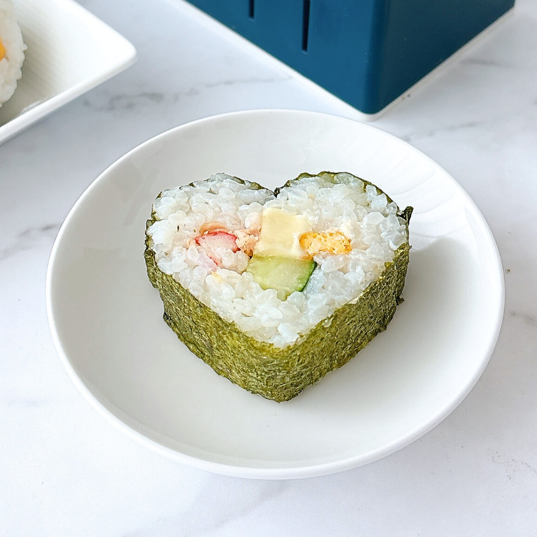 ハート型の寿司ロールが皿に載せられている。海苔で巻かれ、具材としてカニカマ、アボカド、卵が見える。