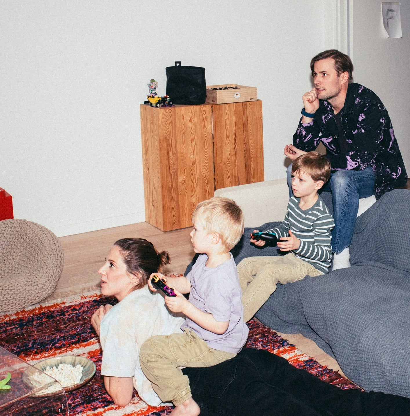 Family sitting on the floor in a living room, focused on video games. Two adults and two children, each holding a game controller