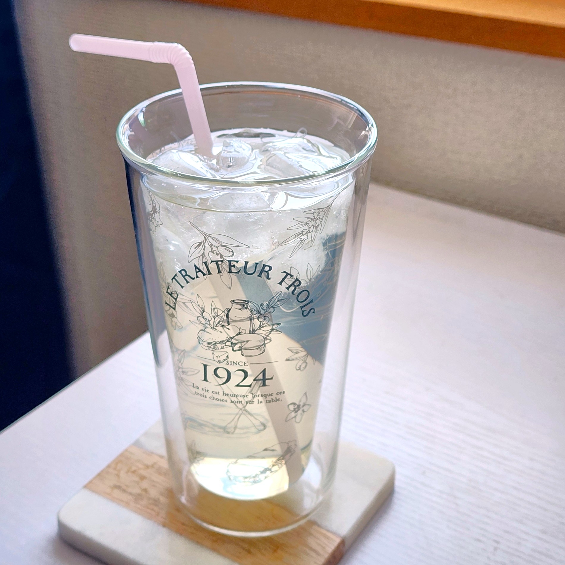 グラスに入ったレモンスカッシュ。氷とストローが添えられている。グラスには「LE TRAITEUR TROIS 1924」と書かれている。