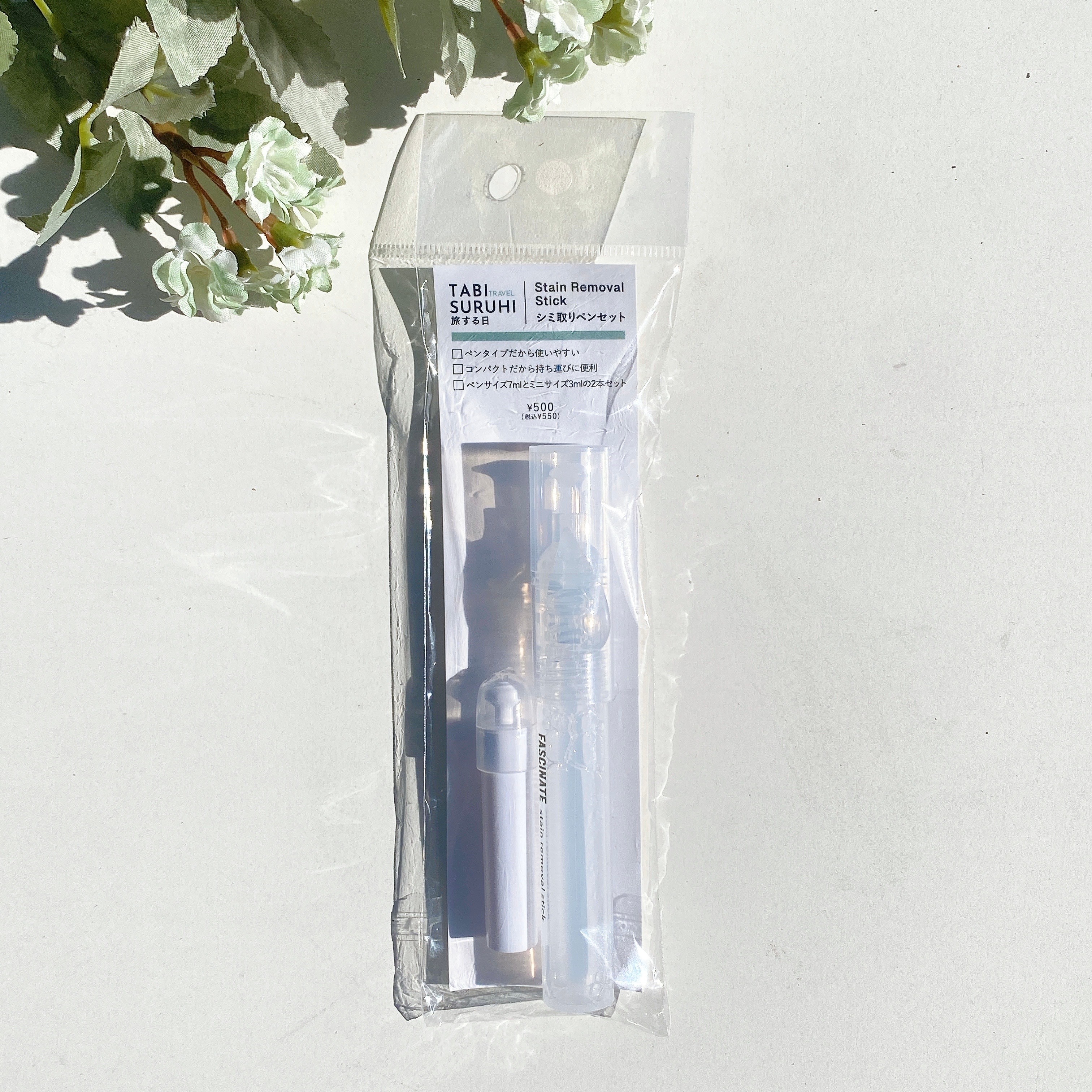 透明な袋に入ったシミ取りセット。棒状のスプレーやペンが含まれている。背景に植物の影が見える。