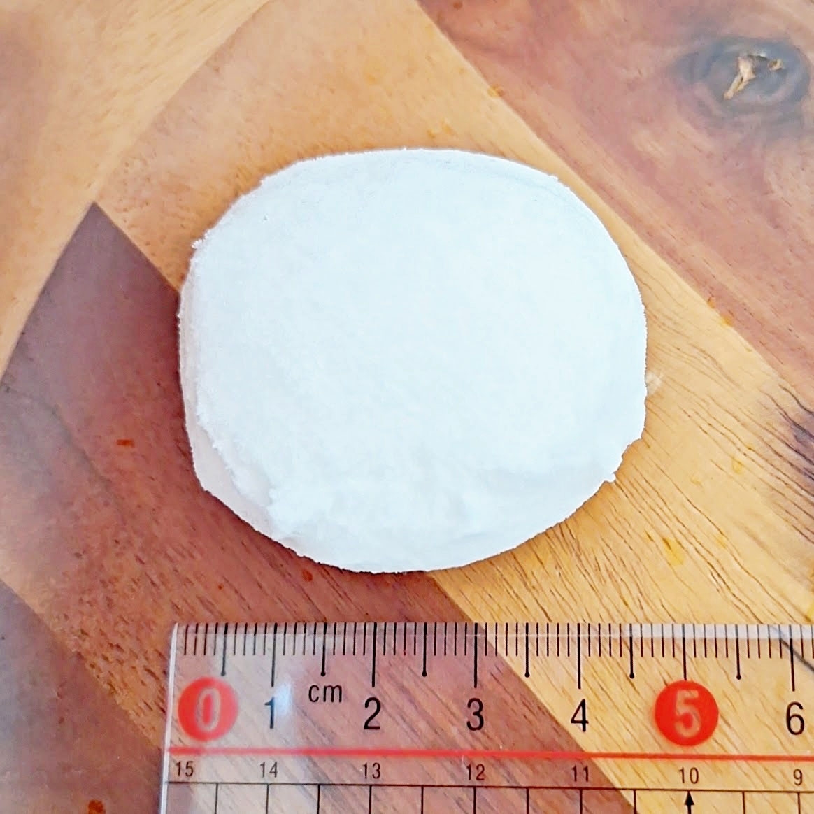 10センチメートルの定規と丸い白い物体が木製の表面に置かれている。