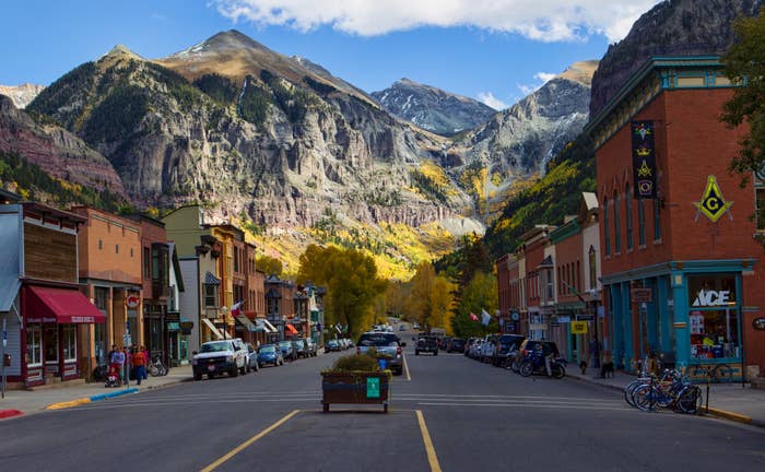 Mountain town street with shops, parked cars, and bicycles. Majestic mountains and trees in the background
