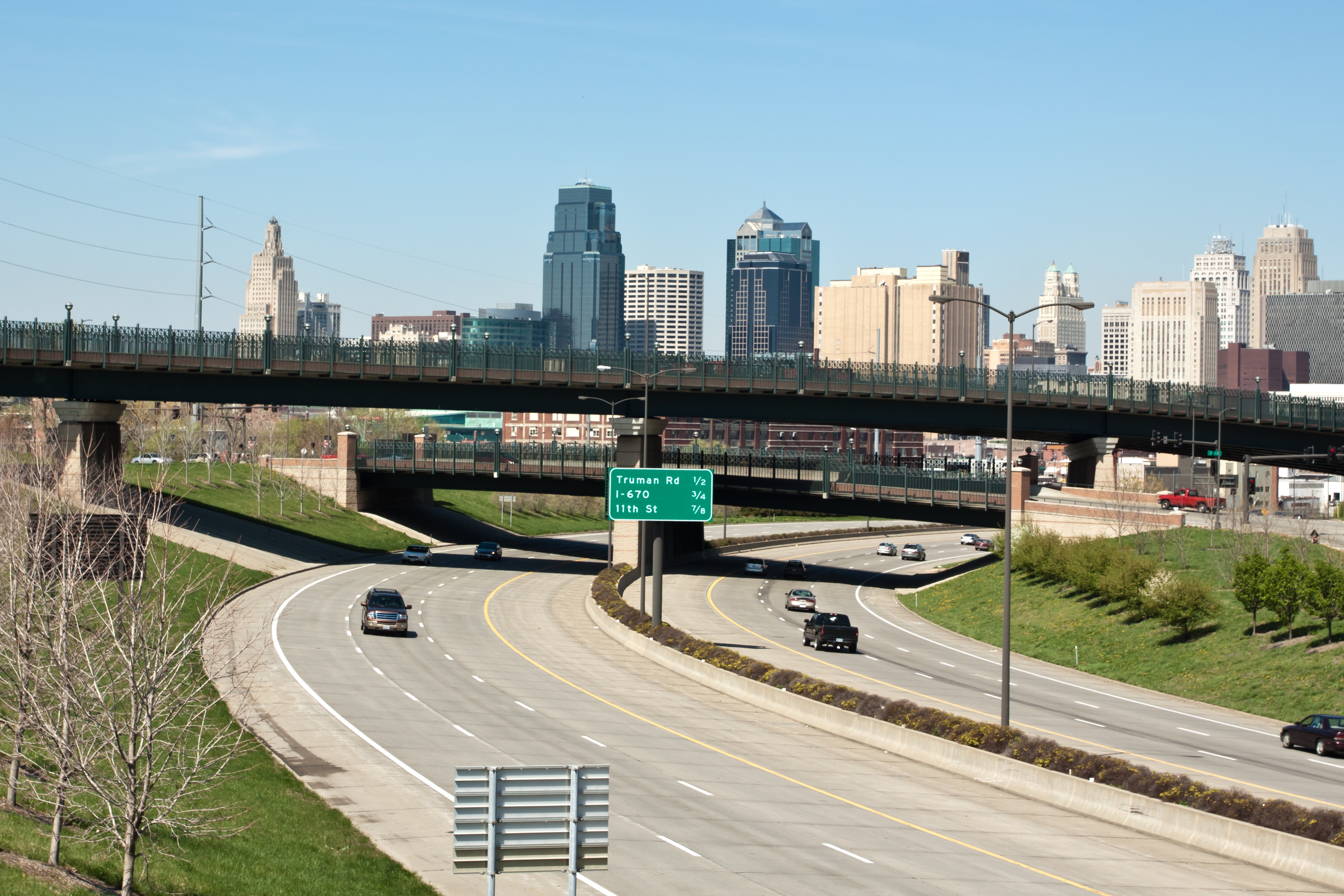 City skyline with tall buildings seen behind a highway overpass, featuring light traffic below