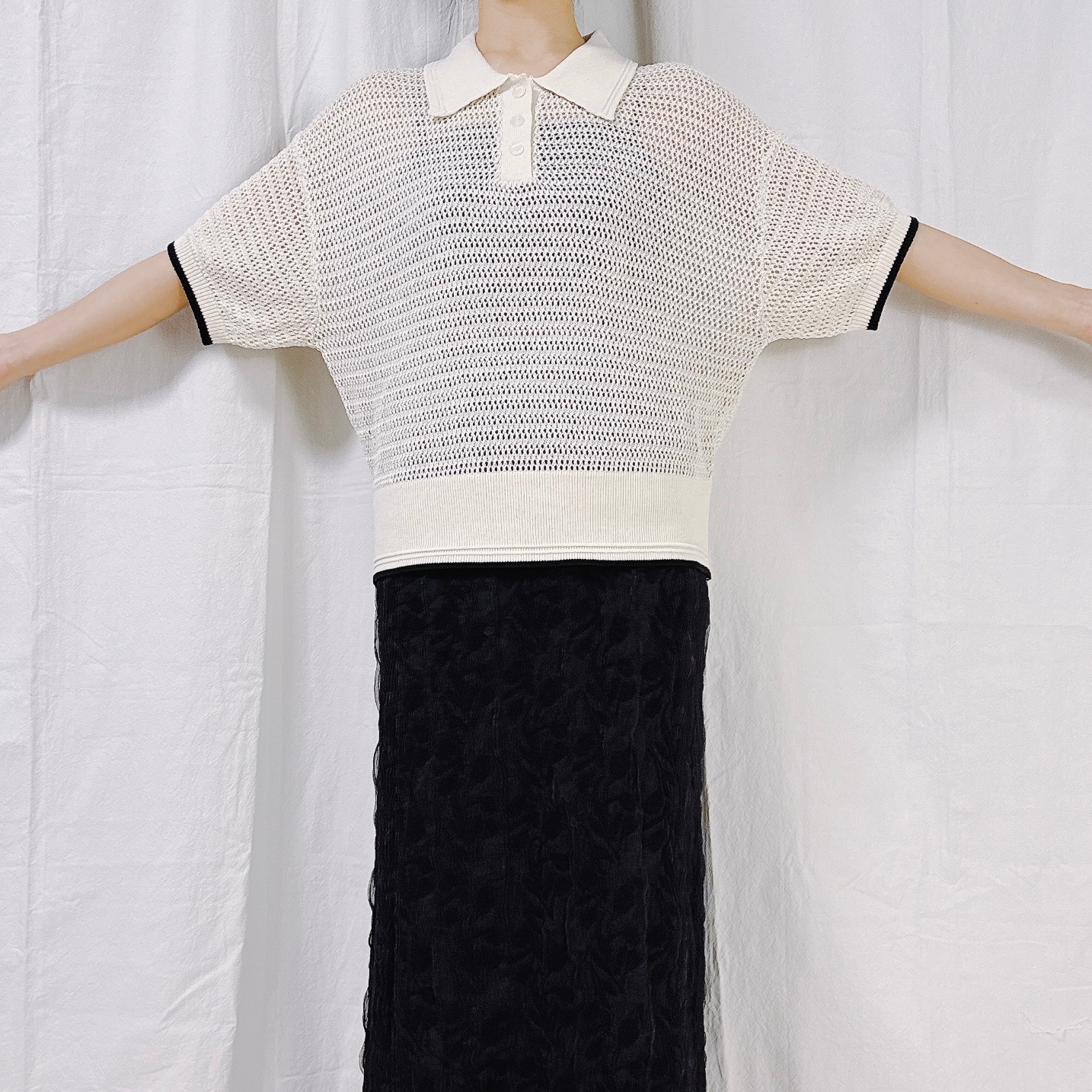 Person wearing a loose-knit short-sleeve sweater and long textured skirt poses with arms outstretched