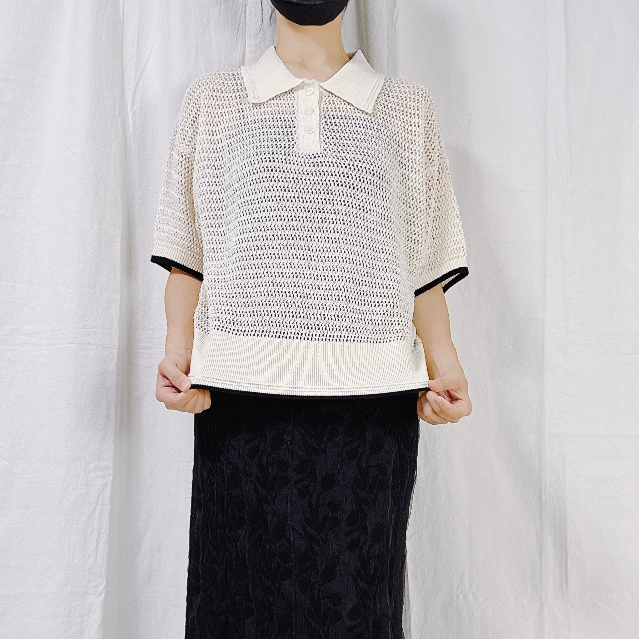 Person wearing a mesh polo shirt and a long, textured skirt, holding the shirt's hem. Face not visible