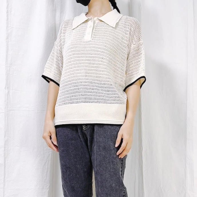 Person wearing a short-sleeve knit polo shirt and jeans poses against a plain backdrop. Face and feet are not visible