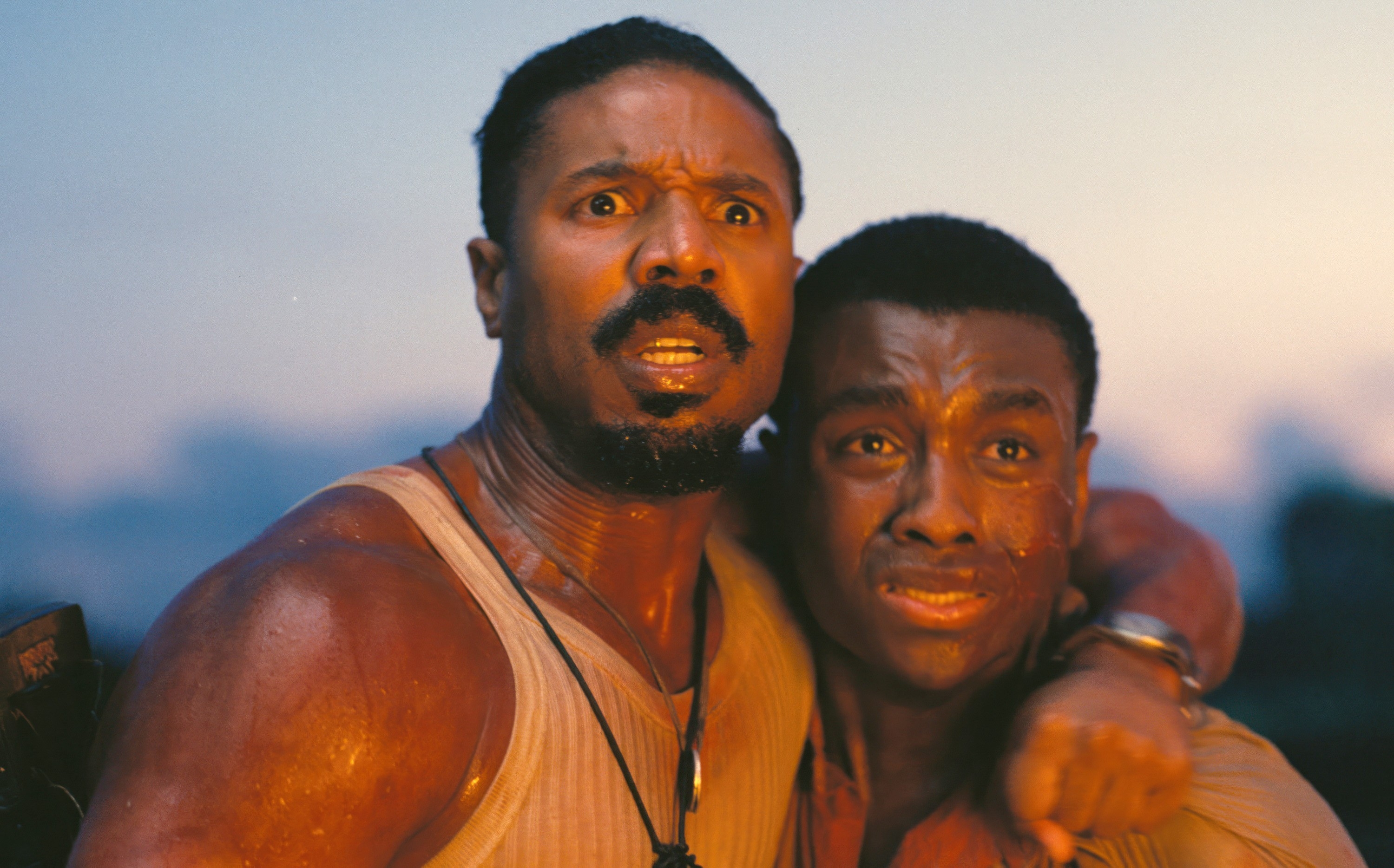 Two men with intense expressions, one wearing a tank top, appear dramatic and emotional, suggesting a pivotal movie scene