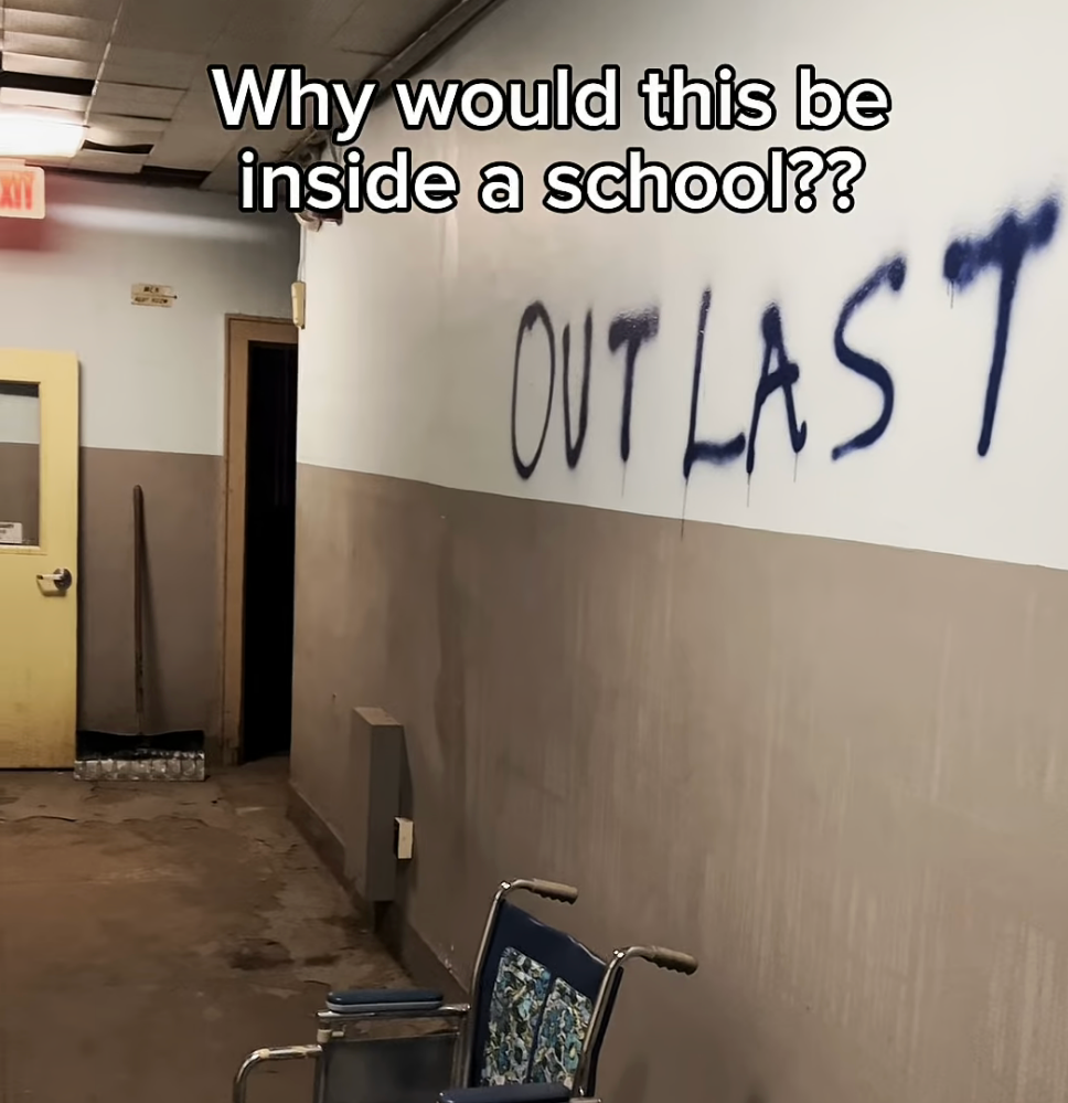 Graffiti reading "OUTLAST" is sprayed on a school hallway wall above an abandoned wheelchair. Text asks, "Why would this be inside a school??"
