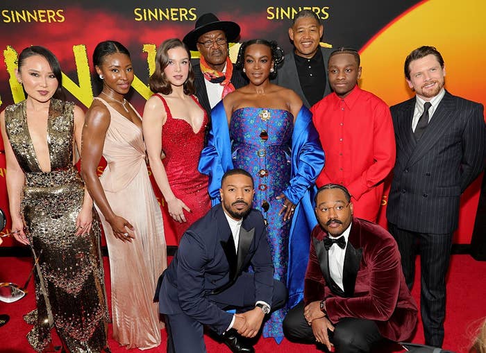 Group of actors in formal wear posed on a red carpet at a premiere