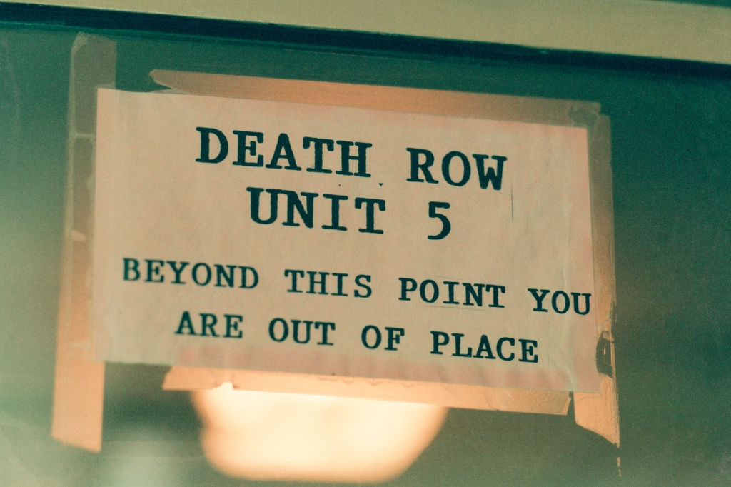 Sign reading "Death Row Unit 5. Beyond this point you are out of place" on a door or window