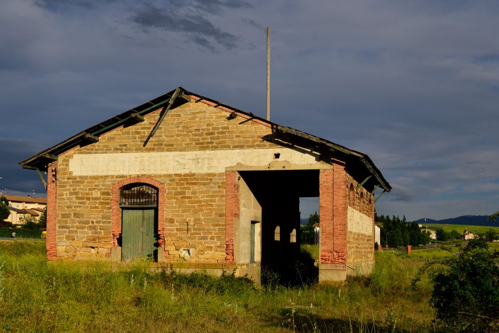 Old brick building with arched doors and windows, surrounded by grass, under a cloudy sky