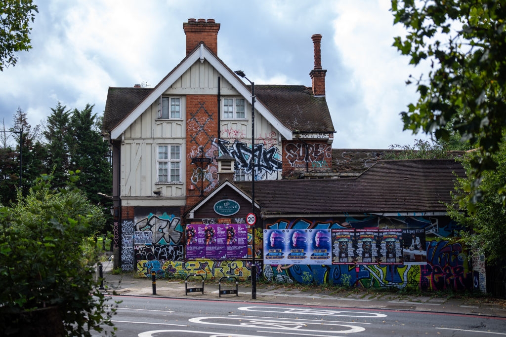 Graffiti-covered building with posters on a city street. The roof has a chimney, and there are trees in the background