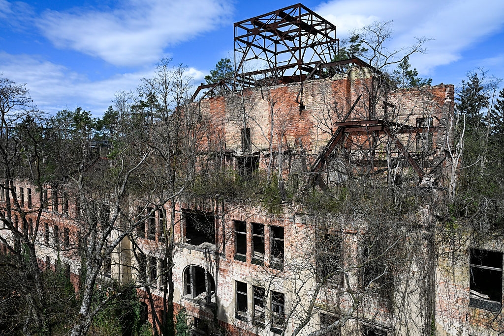 Abandoned brick building in disrepair with overgrown vegetation and a partially collapsed roof structure