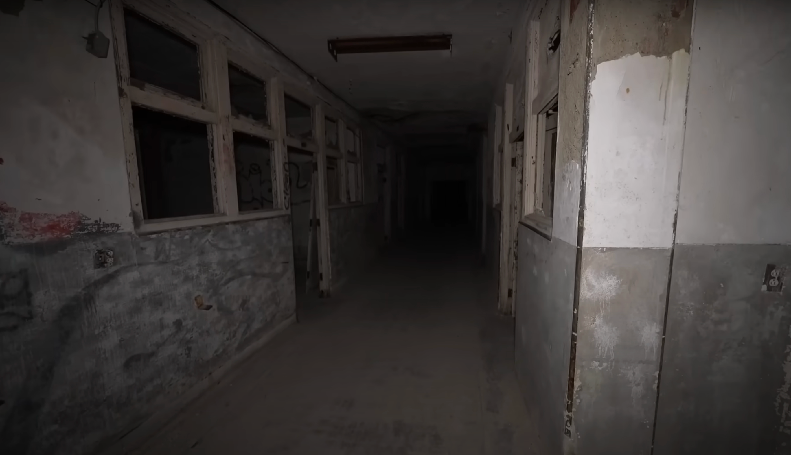 Dark, eerie hallway with peeling walls and broken windows, leading into darkness