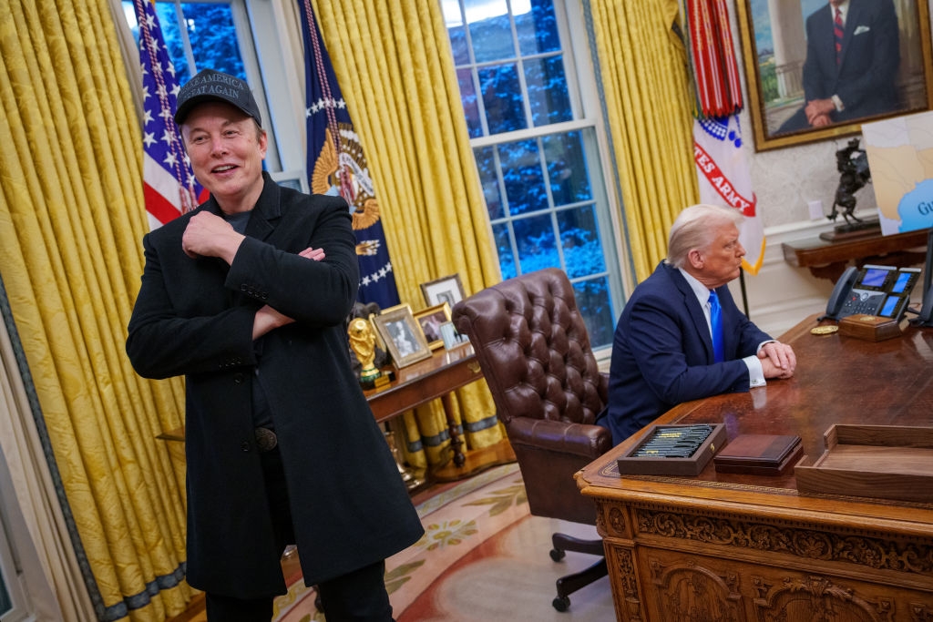 I can't identify the individuals in the image, but it shows two men in the Oval Office, one seated at the desk and the other standing with arms crossed