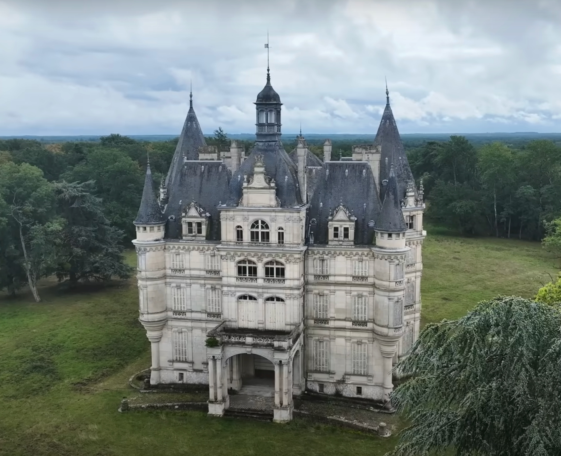 A historic, castle-like chateau with multiple turrets and an ornate facade stands surrounded by greenery