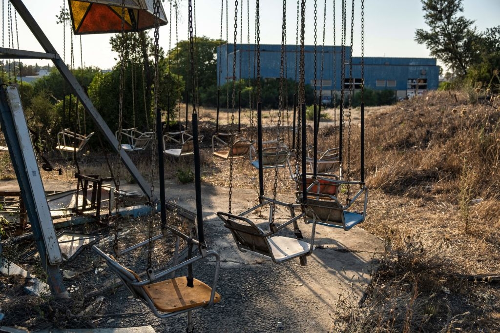 decrepit swing ride at a desolate amusement park, surrounded by dry grass and a large building in the background